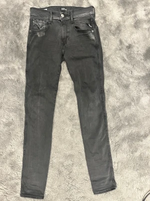 Svarta Replay jeans - Säljer ett par svarta jeans från Replay med klassisk femficksdesign och diskreta slitningar. Jeansen har låg midja och smal passform, perfekta till sneakers eller boots. Materialet är stretchigt för extra komfort.