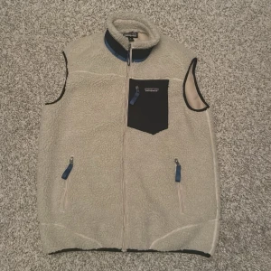 Beige fleeceväst från Patagonia - Snygg fleeceväst från Patagonia med svart bröstficka och blå detaljer på dragkedjorna. Storlek M, i nyskick. Påse finns. Vid fler frågor, skriv gärna privat // AR