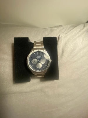 Silverfärgad Regal klocka med blå urtavla - Stilren klocka från Regal med silverfärgat armband i metall och blå urtavla. Klockan har tre mindre urtavlor och tydliga siffror på boetten. Perfekt accessoar för dig som gillar en klassisk men modern look.