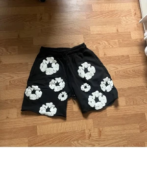 Svarta shorts med vita blommor - Svarta shorts med elastisk midja och stora vita blommönster över hela plagget. Perfekta för en avslappnad och trendig look. Mjukt material och bekväm passform.