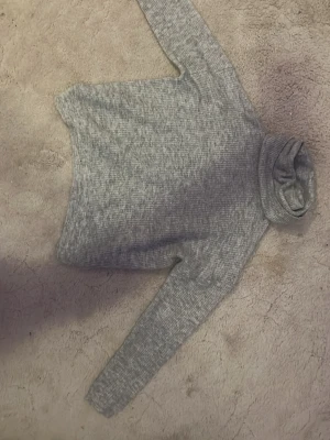 Grå polotröja i ribbstickat - Mysig grå polotröja i ribbstickat material med lång ärm och hög krage. Perfekt för lager på lager och enkel att matcha med olika stilar. Tröjan har en klassisk passform och mjuk känsla. Otroligt mjukt material.