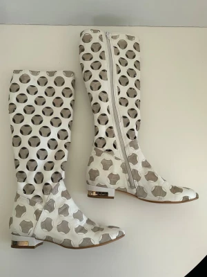 Unika vita stövlar i äkta skinn - Unika vita stövlar i äkta läder från Écolé i storlek 39.  Superfint cirkelmönster i kontrastfärg (beige) med perforeringar, samt bekväm låg klack med gulddetalj. Har sina skavanker här och där (se bilder), men ett par stövlar som du kommer vara ensam om att ha. Älskar dem, men är tyvärr för små för mig. Hoppas de hittar ett annat härligt hem.   Hämtas i Stockholm eller skickas mot porto. 