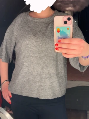 Grå stickad tröja med kort ärm - Mysig grå stickad tröja med rund halsringning och korta, vida ärmar. 