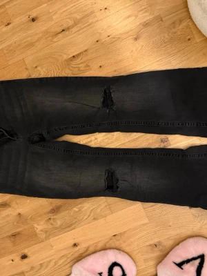 Svarta ripped jeans från Nelly - Snygga svarta jeans från Nelly med slitningar på knäna. Modellen är tight och har klassisk femficksdesign. Perfekta för en trendig och avslappnad stil. Materialet är stretchigt för extra komfort. Används runt 5 ggr är för korta nu.