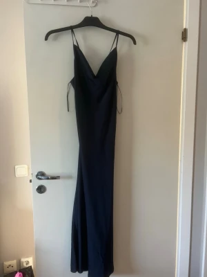 Marinblå balklänning - Marinblå långklänning med tunna axelband ✨  Säljer en elegant marinblå långklänning i mjukt, följsamt material. Klänningen har tunna axelband och en fin ringning framtill samt öppen rygg med knyt-/snördetaljer som ger en snygg och feminin passform.  📏 Passform & längd: Jag är 156 cm lång och på mig går klänningen inte hela vägen ner till fötterna. (Se sista bild för att se hur lång den är på mig) storlek 42 som passar mig med lite större byst och blir en lös passform för mig med storlek S/M 