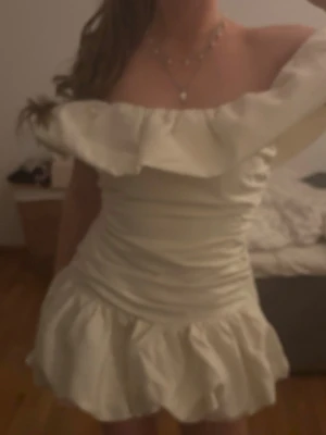 Krämvit kort volangklänning - NYPRIS 550. Supersöt krämvit kort klänning med volangdetaljer och bred offshoulder-krage. Helt ny med prislapp för ja råka beställa två st. Uk storlek 10 vilket e typ 36-38 