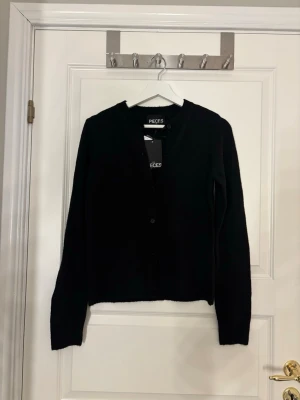Svart kofta från Pieces med knappar - En stilren svart kofta från Pieces med knäppning framtill. Klassisk rak passform och långa ärmar. 
