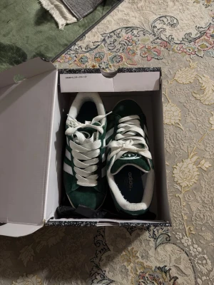 Gröna Adidas sneakers med vita ränder - Snygga gröna Adidas sneakers med klassiska vita ränder på sidorna och vita skosnören. Ovandelen är i mockaliknande material och sulan är vit. Perfekta för dig som vill ha en retro och sportig look.