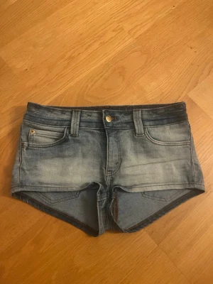 Blå denimshorts från Cheap Monday - Snygga blå denimshorts från Cheap Monday med klassisk femficksdesign och slitna detaljer. Shortsen har låg midja, bälteshällor och en grön logolapp bak. Perfekta för sommaren och ger en avslappnad look.