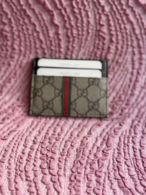  korthållare  - Snygg korthållare  i beige canvas med klassiskt och en grön-röd rand i mitten. Kompakt och smidig design med plats för flera kort. Perfekt accessoar för dig som gillar lyxiga detaljer och stilren look.