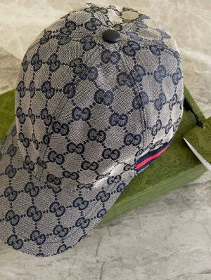 Gucci keps med GG-mönster - Snygg keps från Gucci i beige och marinblått med det klassiska GG-monogrammet över hela kepsen. Kepsen har en böjd skärm och en detalj med röd och marinblå rand på sidan. Tillverkad i canvasmaterial som ger en exklusiv känsla.