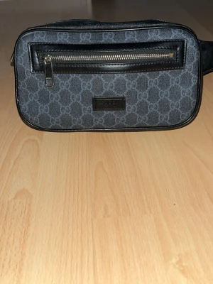  Gucci magväska äkta  - Säljer en svart ryggsäck från Gucci med klassiska röda och marinblå ränder på axelremmen. Väskan har detaljer i silverfärgad metall och dragkedjor med Gucci-logga. Materialet är en mix av slitstark nylon och läderdetaljer. Perfekt för dig som gillar exklusiv och stilren design.äkta bra skick 