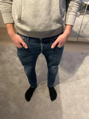 Dondup jeans - Säljer ett par blå dondup jeans med snygga slitningar och tvättade detaljer. Jeansen har klassisk femficksdesign, låg midja och smal passform. Perfekta för en avslappnad och trendig look. Materialet är troligtvis bomull med lite stretch.