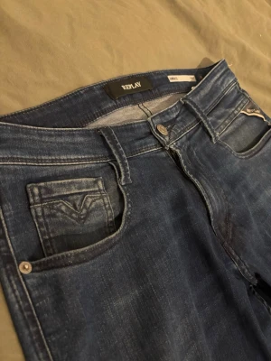 Mörkblå Replay Anbass W29 - Snygga mörkblå jeans från Replay, modell Ambass. Klassisk femficksdesign med Replay-logga på fickan och slitningar för en cool look. Jeansen har smal passform och är tillverkade i stretchigt denim för extra komfort. W29 L30