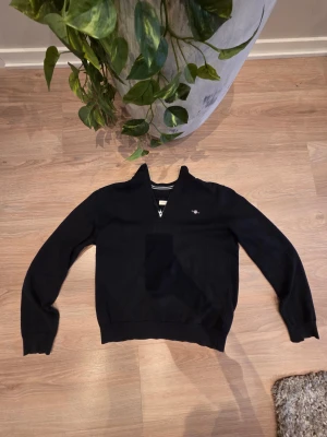 Mörkblå  half zip tröja från Gant - Svart långärmad tröja från Gant med half zip och liten broderad logga på bröstet. Tröjan har ribbade muddar och krage med diskreta ränder på insidan. Perfekt för dig som gillar klassisk och stilren design. ✨️