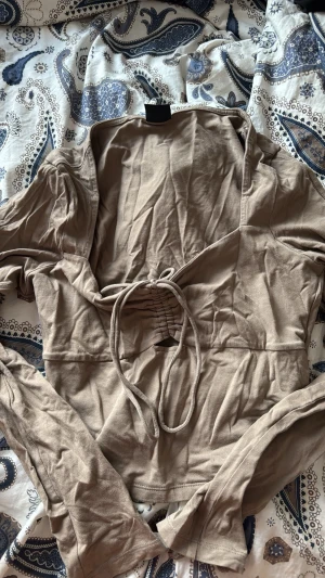 Beige omlottopp med knytband - Trendig beige omlottopp med långa ärmar och knytband i midjan. Toppen har en v-ringad design och är tillverkad i mjuk bomull, perfekt för en avslappnad men snygg look.