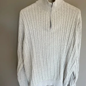  half zip-tröja Lindbergh - Snygg ljusgrå stickad tröja från Lindbergh med relaxed fit. Tröjan har kabelstickat mönster, hög krage och half zip-dragkedja. Perfekt för dig som gillar en clean och stilren look 