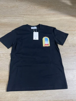 Svart t-shirt  - Svart t-shirt  med rund hals och tryck på bröstet i form av ett fönster med blå och röda detaljer samt texten T-shirten har en klassisk passform och är tillverkad i mjuk bomull.