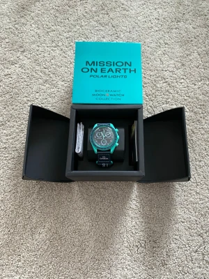 Omega x Swatch MoonSwatch Polar Lights - Säljer en Omega x Swatch Speedmaster MoonSwatch 'Mission on Earth: Polar Lights' med turkos boett i biokeramik och svart urtavla. Klockan har kronograf, tachymeter och svart textilband med Omega-logga. Levereras i originalförpackning.