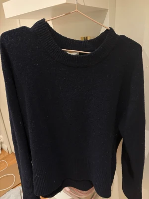 Marinblå stickad tröja - Mysig mörkblå stickad tröja med rund halsringning och ribbade muddar vid ärmslut och nederkant. Tröjan har en enkel, klassisk design och är perfekt för lager på lager under kyliga dagar. Passar till både jeans och kjol.