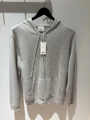 Grå cashmere hoodie John Henric - Mjuk och lyxig grå hoodie i cashmere från John Henric. Hoodien har dragkedja framtill, justerbar huva med snören och två fickor. Perfekt för dig som vill ha en stilren och bekväm look med exklusiv känsla.