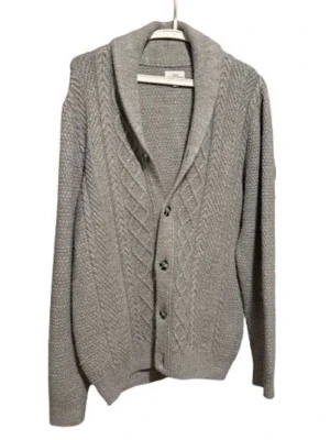 Grå kabelstickad kofta med sjalkrage - Grå kofta med kabelstickat mönster framtill, sjalkrage och knäppning med fyra knappar. Långärmad och tillverkad i ett mjukt, tjockare material som passar perfekt när det är kyligt. Klassisk och stilren design.