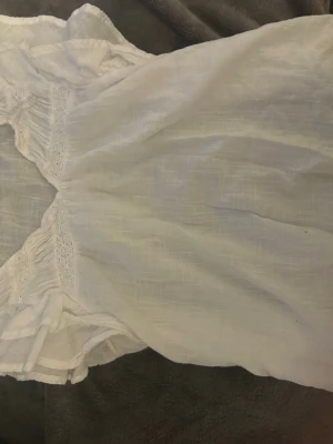 Vit blus med spets från Lindex - Söt vit blus från Lindex med fina spetsdetaljer framtill och volang vid ärmslut. Blusen är tillverkad i ett lätt och luftigt tyg, perfekt för en fräsch och stilren outfit 