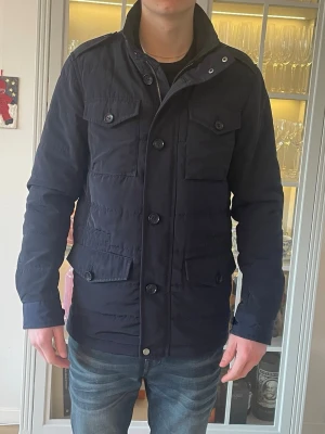 Mörkblå Riley Fieldjacka - XS/S - Jag säljer den här riktigt snygga fieldjackan från Riley i storlek 44 vilket motsvarar ungefär XS/S. Den har inte använts mycket och har inga defekter. Nypris låg på ca 1999kr hos Brothers och jag säljer den för 799kr. Tveka inte att höra av er!