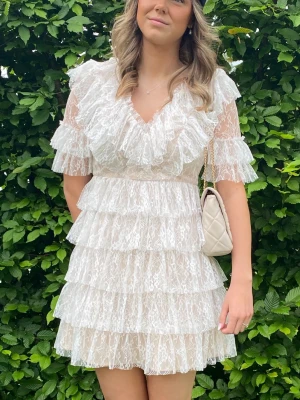Vit volangklänning i spets - Superfin kort vit klänning med flera lager volanger och spetsdetaljer. Klänningen har v-ringning och korta ärmar. Köpte för 2800kr och enbart använd på min student.🥰