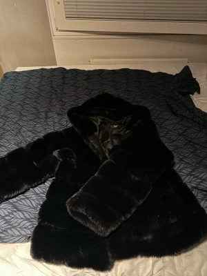 Svart pälsjacka med huva YXFS - Snygg svart pälsjacka från YXFS med stor huva och glansigt innerfoder. Jackan har en fluffig och lyxig känsla, perfekt för kalla vinterdagar. Klassisk rak modell, den är som ny då jag endast använt den 3-4 gånger. Den är köpt från jackie och är i storlek XL, Nypris på jackan är 1000kr😊