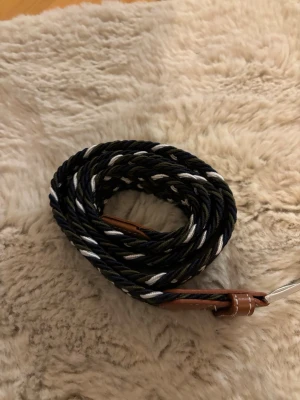 Svart och vit flätat bälte - Snyggt flätat bälte i svart och vitt med bruna skinn-detaljer vid spännet. Bältet har ett klassiskt silverfärgat spänne och passar perfekt till jeans eller chinos. Den flätade designen gör det enkelt att justera längden efter behov.