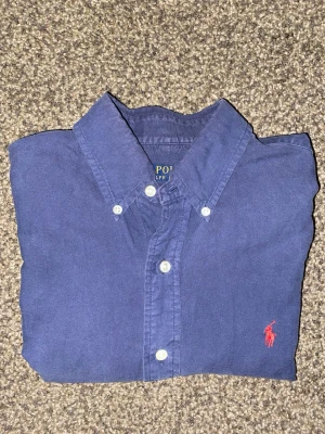 Mörkblå Ralph Lauren skjorta - Mörkblå Ralph Lauren skjorta i storlek S med slim-fit passform. Button-down krage med back collar knapp. Inga defekter utöver stygnen på tvättlappen, använd ett fåtal gånger. 9/10 skick