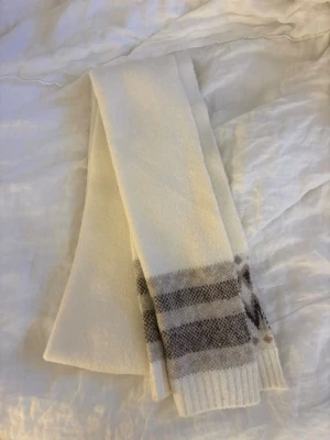 Vit halsduk från lager 157 med mönster - Mysig vit halsduk från lager157 med beige & brunt rutmönster i ändarna. Halsduken är stickad och har ribbade kanter. Perfekt för kalla dagar och enkel att matcha med olika outfits.