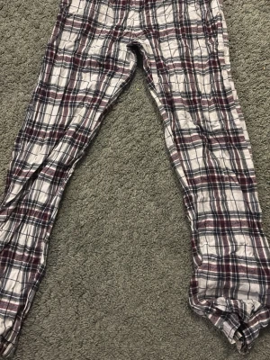 Rutiga pyjamasbyxor i bomull - Mysiga pyjamasbyxor med rutigt mönster i vitt, vinrött och mörkblått. Tillverkade i mjuk bomull med avslappnad passform och resår i midjan. Perfekta för chillkvällar hemma.