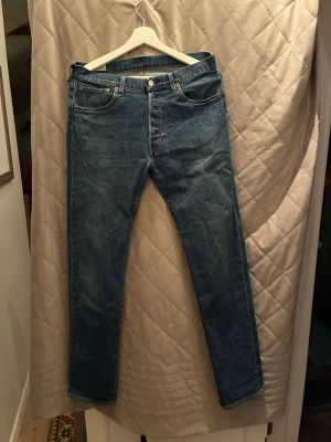  Levi's jeans 501 - Säljer ett par klassiska blå jeans från Levi's med rak passform. Jeansen har fem fickor, knappgylf och den ikoniska läderpatchen bak i midjan. Tillverkade i slitstark denim med snygg tvättad look. Storleken är W31/L34. 