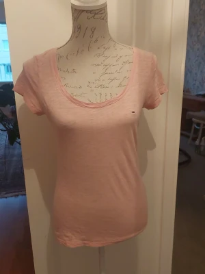 Ljusrosa t-shirt från Tommy Hilfiger - Ljusrosa t-shirt från Tommy Hilfiger med liten logga på bröstet. T-shirten har rund halsringning och korta ärmar. Tillverkad i mjuk bomull och har en slim passform.