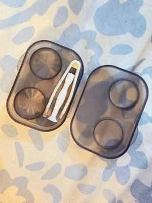 Svart linsfodral med pincett - Praktiskt svart linsfodral i plast med två fack för linser och en vit pincett för enkel hantering. Perfekt att ha med i väskan eller på resan för att förvara kontaktlinser smidigt och hygieniskt.