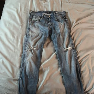 Blå Replay jeans med slitningar - Snygga blå jeans från Replay med slitna detaljer på knäna och coola bakfickor med svart broderi. Jeansen har klassisk femficksdesign, normal passform och är tillverkade i mjukt denimtyg. Perfekta för dig som gillar en avslappnad och trendig look.