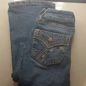 Blå jeans från Gina Tricot med broderi - Snygga blå jeans från Gina Tricot i storlek 158. Jeansen har dekorativa broderier och mönstrade detaljer på bakfickorna samt klassisk femficksdesign. Tillverkade i jeansmaterial med kontrastsömmar och knappstängning framtill.