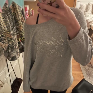 Grå sweatshirt från Victoria's Secret - Supermjuk grå sweatshirt från Victoria's Secret med glittrigt silvrigt tryck framtill. Tröjan har en avslappnad passform, bred halsringning och långa ärmar. Perfekt för chill dagar eller när du vill vara extra comfy.