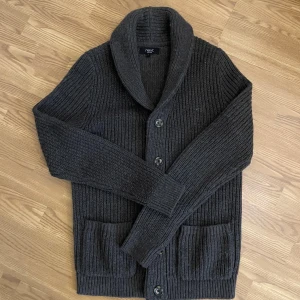 Mörkbrun stickad kofta  - Säljer en HELT NY mörkbrun stickad kofta från Next i storlek S, med grov ribbstickning, sjalkrage och stora knappar framtill. Koftan har två rejäla fickor och lång ärm, perfekt för kyliga dagar. Snygg och enkel att matcha med jeans eller t-shirt. (Modell 176cm, 70kg) 