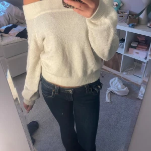 Offshoulder vit stickad tröja - Superfin vit stickad tröja med offshoulder-modell och långa ärmar. Tröjan har bred ribbad kant upptill och vid midjan, vilket ger en snygg och avslappnad passform. Perfekt för dig som gillar en stilren och mysig look. Ganska nopprig 