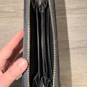 Svart plånbok med ormmönster - Snygg svart plånbok med ormmönstrad yta och dragkedja runtom. Plånboken har flera fack för kort, mynt och sedlar samt en praktisk handledsrem. Perfekt för dig som vill ha stilren och trendig accessoar med plats för allt viktigt.