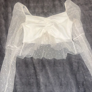 Vit meshblus med puffärmar från Boohoo - Supersöt vit blus från Boohoo med transparenta meshärmar och volangkant. Toppen har prickigt mönster i tyget, rynkdetalj framtill och croppad passform. Perfekt för dig som gillar romantisk och trendig stil.