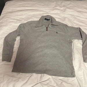 Grå half zip tröja från Polo Ralph Lauren - Snygg grå långärmad tröja från Polo Ralph Lauren med half zip och klassisk krage. Tröjan har en liten broderad logga på bröstet och är gjord i mjuk bomull. Perfekt för lager-på-lager och chill vardagsstil.
