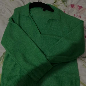 Grön stickad tröja med krage från Lindex - Grön stickad tröja från Lindex med klassisk krage och v-ringning. Tröjan har långa ärmar och breda ribbade muddar vid ärmslut och nederkant. Perfekt för dig som vill ha en färgklick i garderoben.