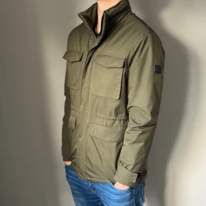 J Lindeberg Fieldjacket - Urfet fieldjacket ifrån J.Lindeberg i storlek L | modellen är 185 cm lång och väger ca 77 kg och den sitter bra | fint skick, bara att loggan på ärmen är lite skrapig men det ser man inte eller tänker på i lite längre avstånd.