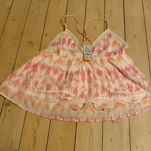 Mönstrad linnetopp från Gina Tricot Young - HELT OANVÄND!!Säljer en superfin linnetopp från Gina Tricot Young med tunna axelband och broderade detaljer. Toppen har ett rosa, vit och gult abstrakt mönster, spets vid bysten och broderade inslag nertill. Perfekt för varma dagar och somriga vibes! Nypris: 299 Mitt pris:190