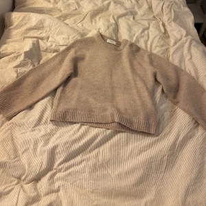 Beige stickad tröja från Gina Tricot - Mysig beige stickad tröja från Gina Tricot i ullblandning. Tröjan har en klassisk rund halsringning, ribbade muddar och en något croppad passform. Perfekt för lager-på-lager under kyliga dagar.