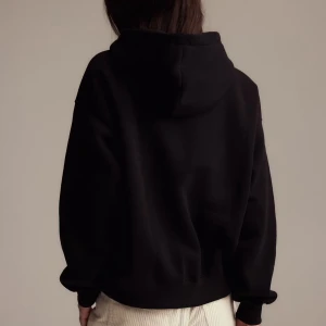 Svart hoodie - En svart hoodie med huva och långärmad design. Tröjan har en avslappnad passform och är perfekt för kyligare dagar. Tillverkad i mjukt material som känns skönt mot huden. Enkel och stilren look som passar till det mesta.
